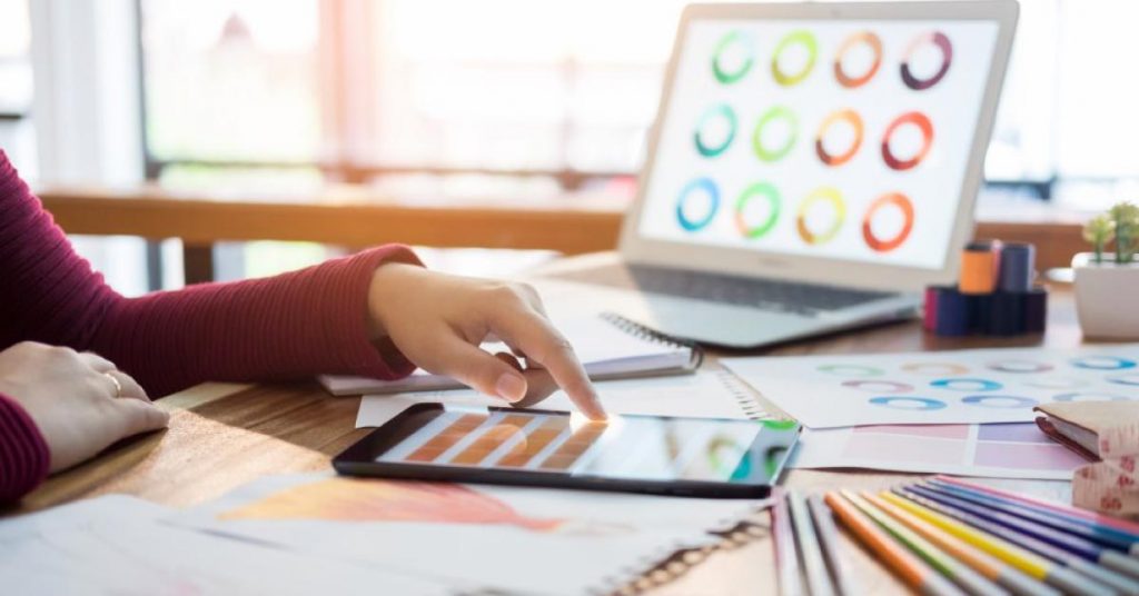 mulher trabalhando no tablet e no notebook, dando um exemplo de economia criativa