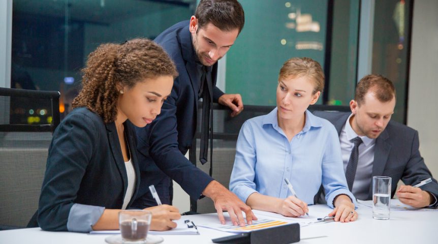Business people sitting in conference room and discussing business issues. Executive manager standing, pointing to document and explaining his idea to business team