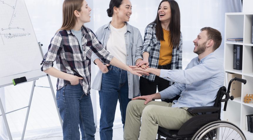 Mulheres cumprimentando um homem cadeirante, exemplificando o conceito de acessibilidade digital.