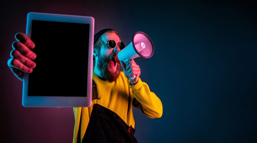 Como funciona o Google Ads Homem segurando um tablet em uma mão e um megafone na outra. Imagem sobre como funciona o Google Ads.