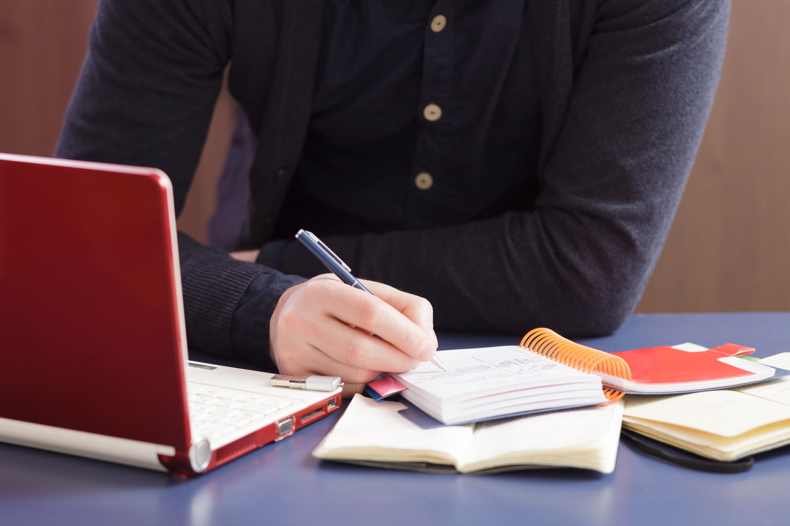 Redator anotando palavras-chave em seu caderno e criando um conteúdo para blog em seu notebook.