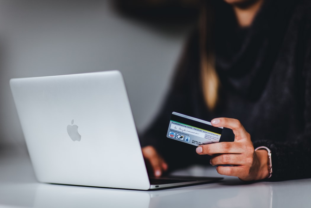 mulher segurando um cartão de crédito em frente ao computador, exemplificando o conceito de vendas online