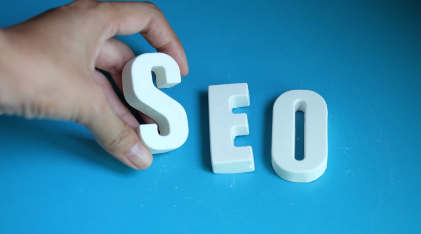 Mão arrumando letras brancas formando a palavra SEO. Imagem ilsutrativa sobre o que é SEO.